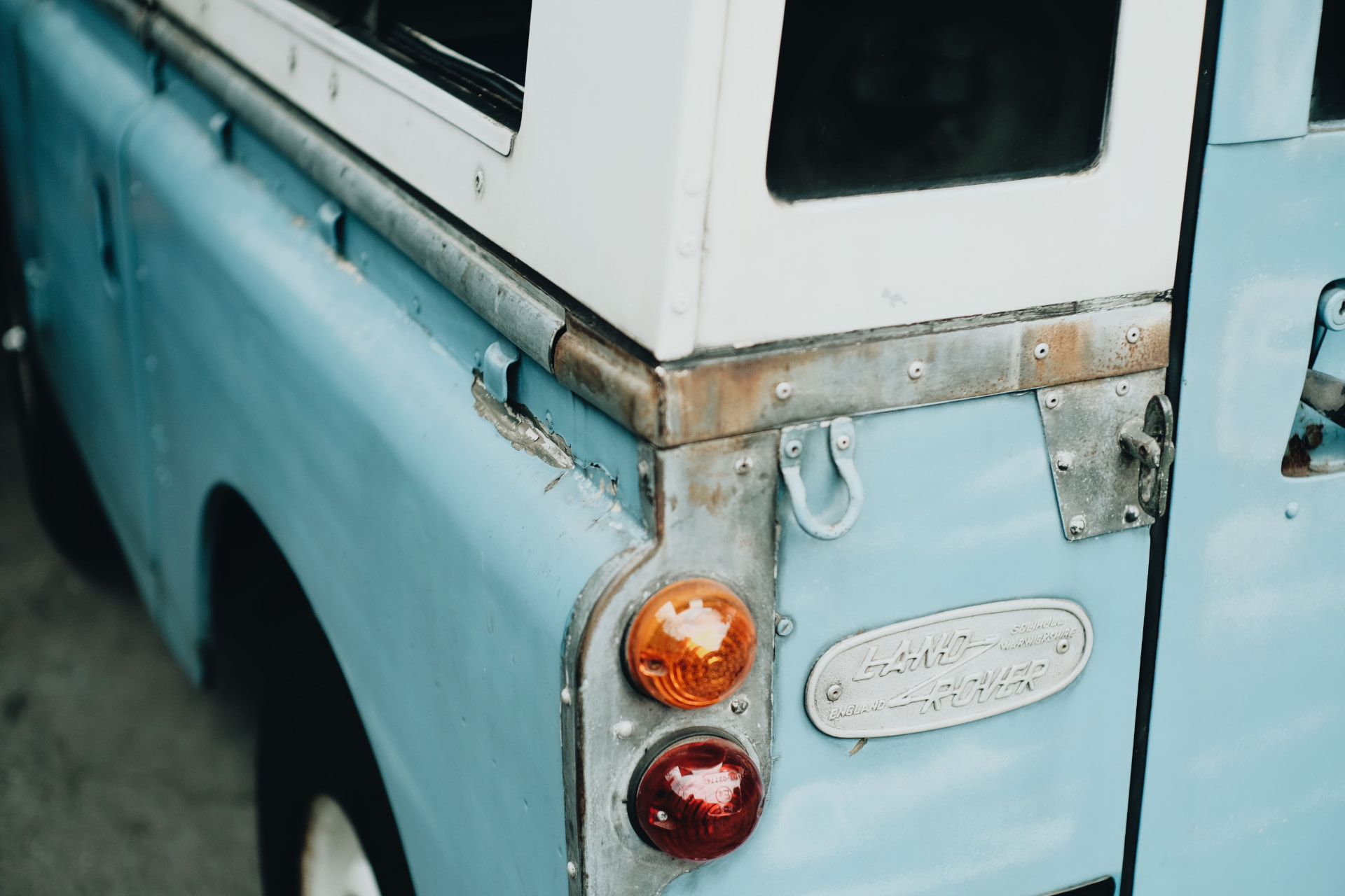 Rear corner of a light blue classic Land Rover with amber and red tail lights